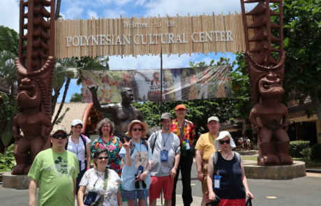 Highlight Vacations travelers standing in front of the Welcome to the Polynesian Cultural Center sign with a statue