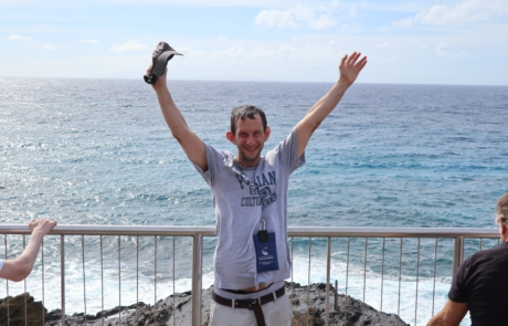 Highlight Vacations traveler raising his legs and smiling in front of the Halona blowhole