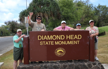 Highlight Vacations travelers posing in back of the Diamond Head State Monument sign