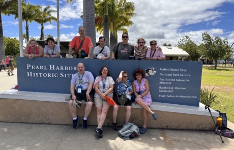 Highlight Vacations travelers and staffs sitting and standing around the Pearl Harbor Historic Site sign.