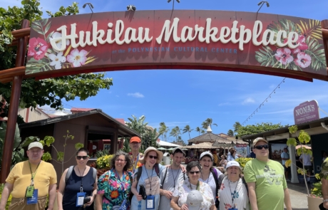 Highlight Vacations travelers standing in front of the Jukilau Marketplace sign at the Polynesian Cultural Center